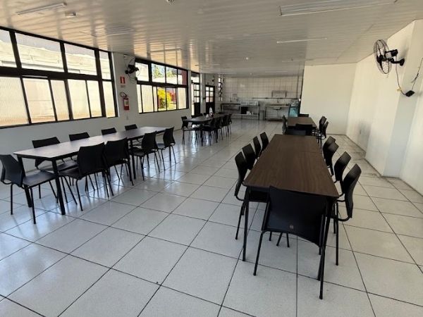 Refeitório corporativo amplo recém reformado com mesas de madeira, cadeiras pretas, piso cerâmico claro e janelas grandes, ambiente comercial iluminado, fotografia realista de interiores